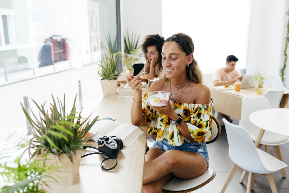 Stylish woman eating and reading book in cafe