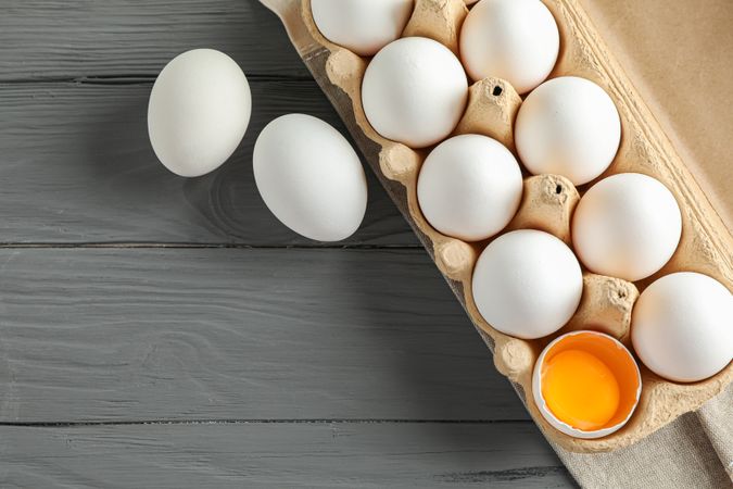 chicken eggs in carton box on wooden table, space for text and top view