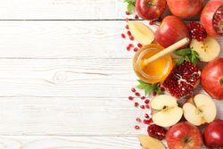 Top view of glass honey pot with dipper, pomegranate seeds, and an apple on right side of table