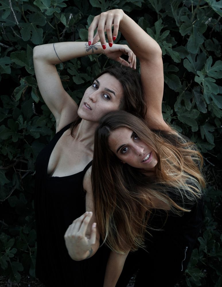 Young women posing near green bush