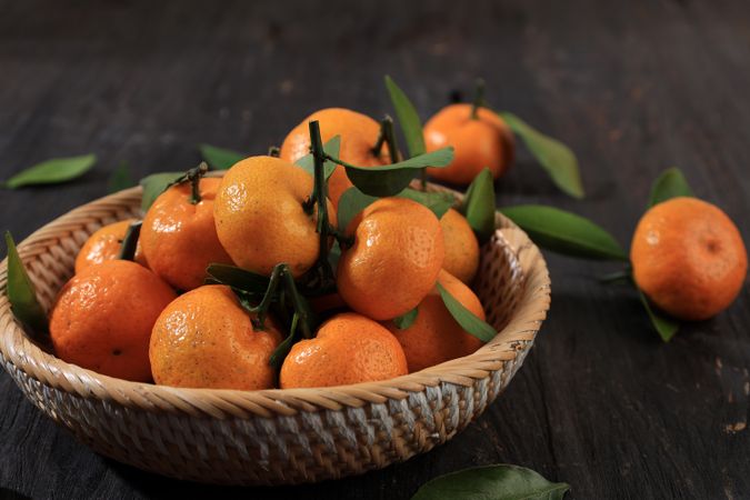 Close Up Fresh Ripe Sicilian Tangerines with Green Leaves in Rattan Bowl