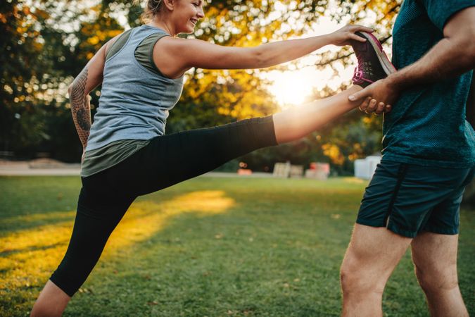 Woman stretching her leg with the support of personal trainer in the park