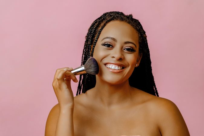 Smiling Black woman holding make up brush to her cheek with eyes closed