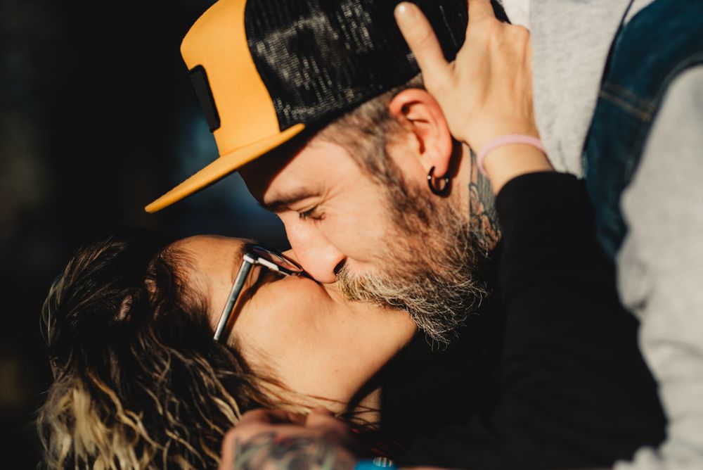 Happy couple hugging and kissing near tree in park