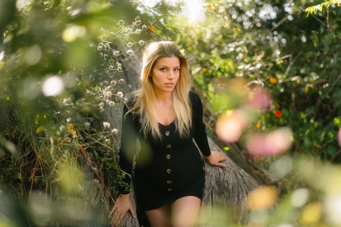 Pensive pregnant woman looking at camera while sitting in garden in sunny day