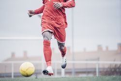 Black soccer player with red outfit playing soccer.
