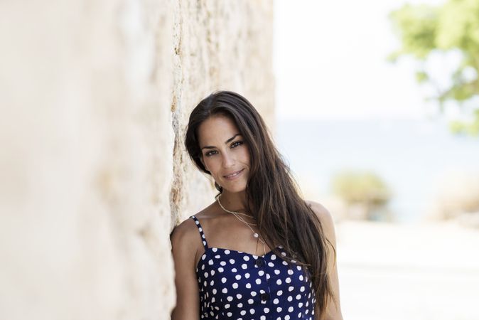Beautiful hispanic woman in blue dress leaning head on wall and looking at camera