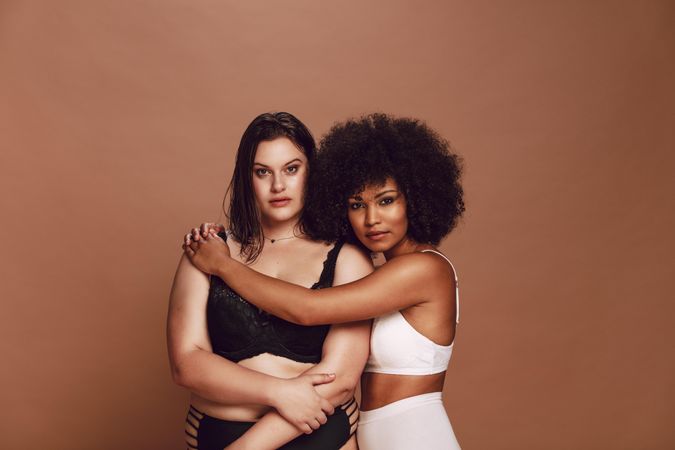 Black model hugging white woman against brown background