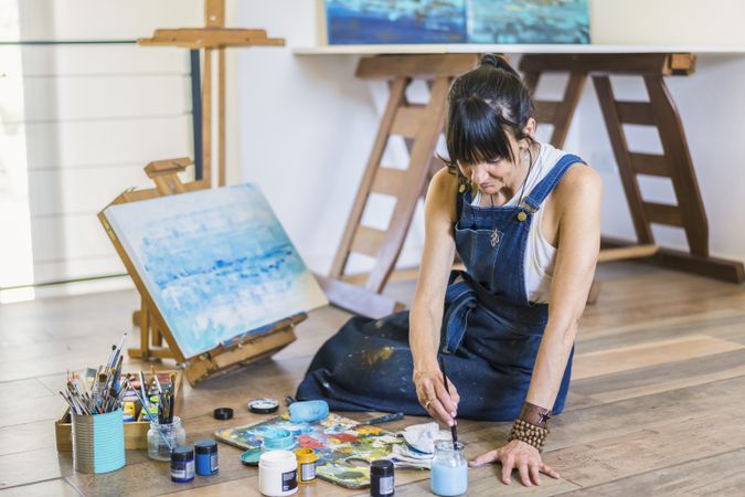 Woman artist painting on a canvas a blue abstract painting. Creative ywoman working on the floor in her art studio.