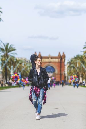 Front view of a young laughing hipster woman walking in a park in sunny day while looking away