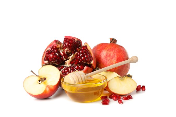 Side view of pot of honey with dipper, split pomegranate and apples