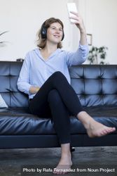Barefoot brunette woman sitting on the sofa using smartphone bDjZzQ