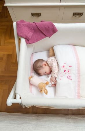 Baby sleeping in a cot with pacifier and toy