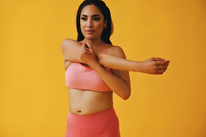 Hispanic female in yoga clothes stretching her arm in yellow studio