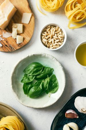 Basil leaves and ingredients for pesto sauce on plates on table