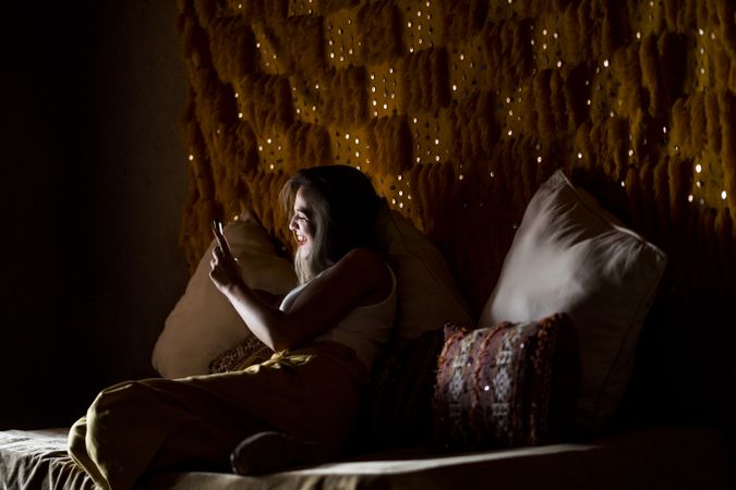 Smiling woman using smartphone in dark room
