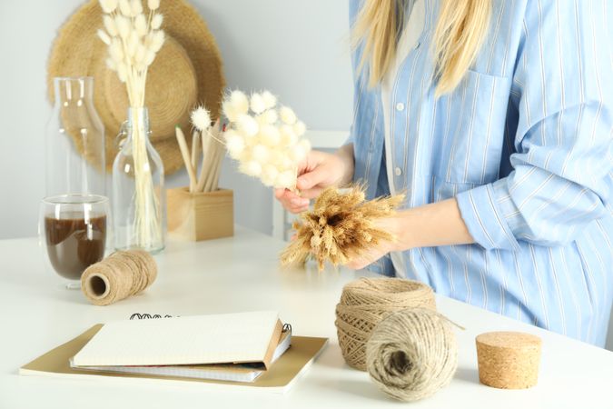 Woman in blue striped shirt crafting a dried floral arrangement in stylish work space