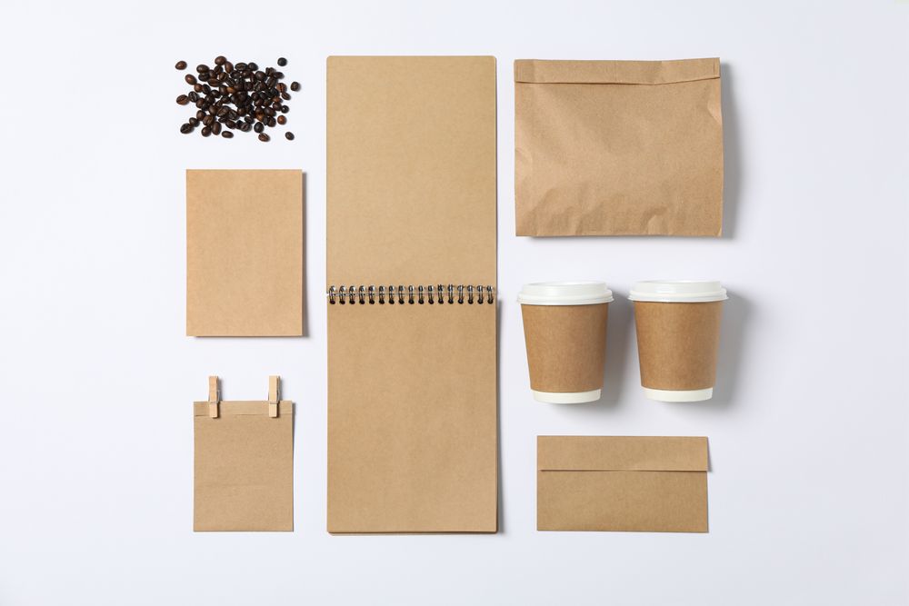 Flat lay. Blank stationery, paper cups and bunch of coffee on plain background, mockup