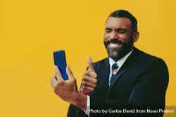 Smiling Black businessman in suit speaking at smartphone screen while giving the thumbs up bY96gb