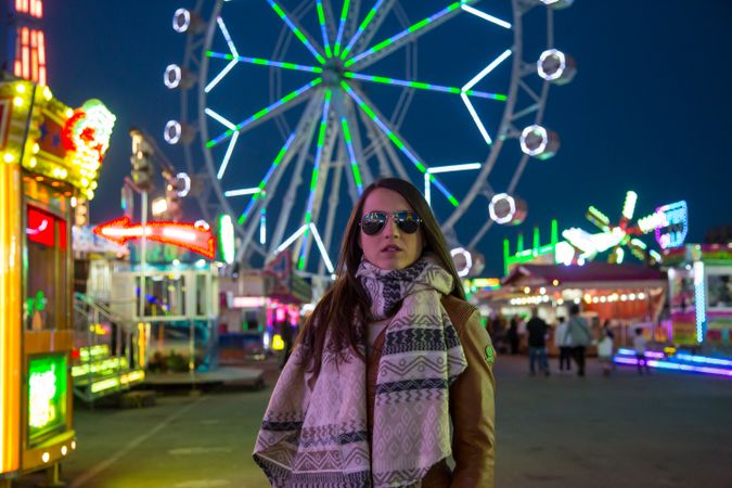 Smiling young woman near illuminated ferris wheel at night