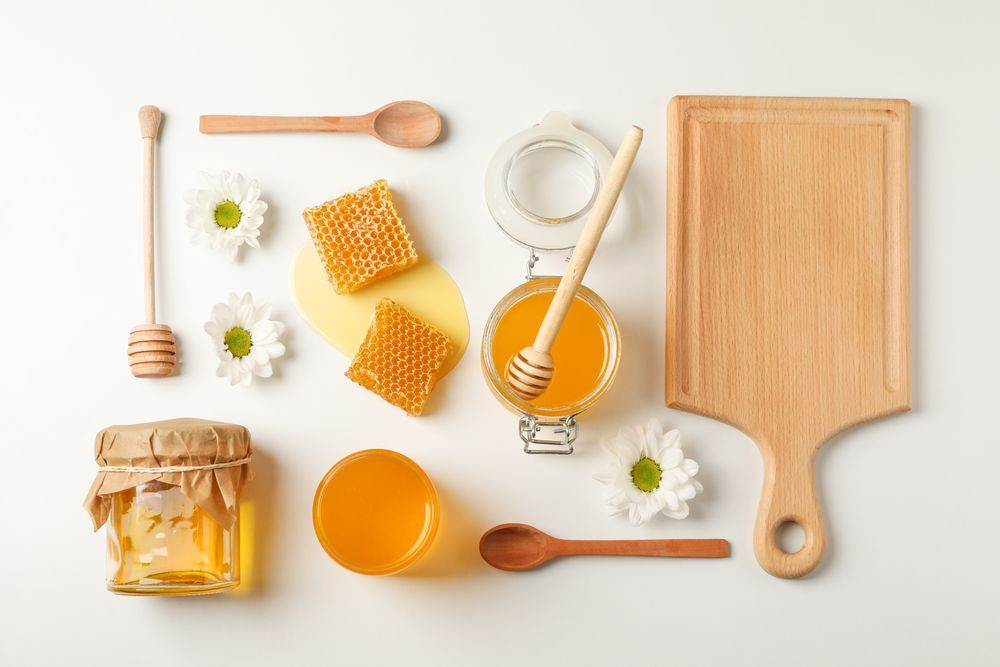 Flat lay. Honey, dipper, spoon and board on neutral background, space for text