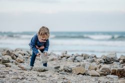 Smiling child near heap of stones on shore near water