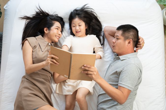 Top view of parent reading book with daughter on bed. happy family enjoy spending time together. Love bonding and insurance concept