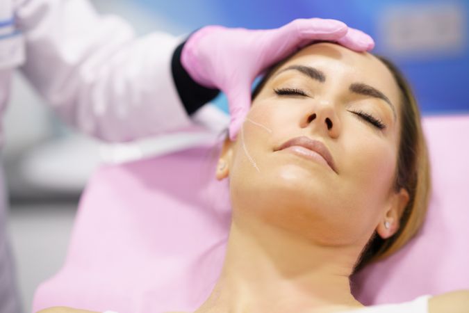 Woman having side of face prepared for cosmetic treatment