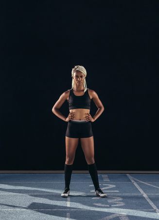 Female athlete standing at the start line on running track on a dark background