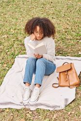 Black Latina female reading book in park