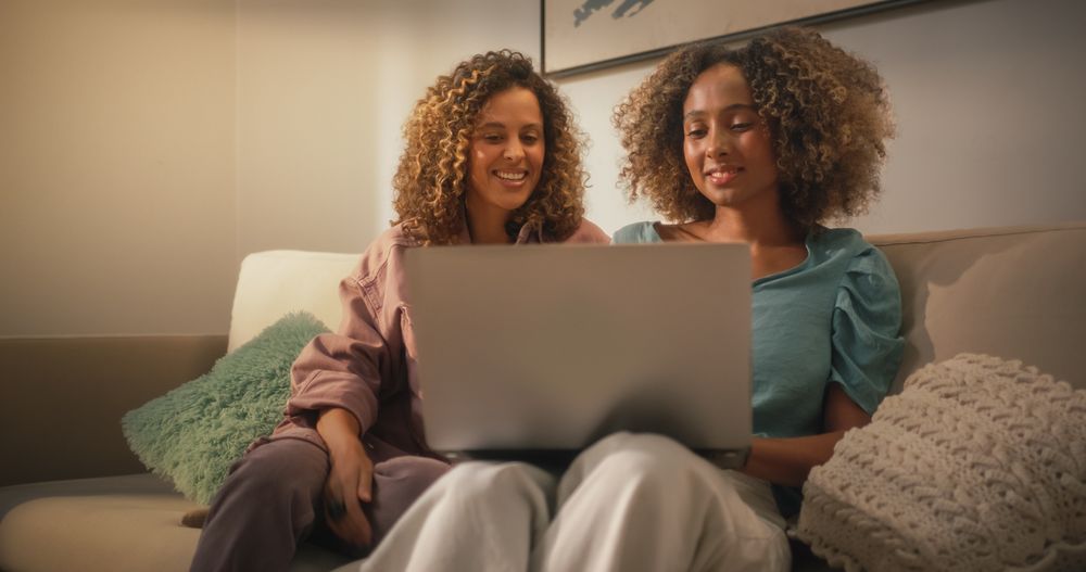 Portrait of Two Brazilian Young Women Using Laptop Computer While Sitting on a Sofa at Home.