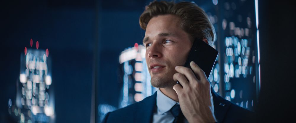 Close Up Portrait of White Businessman in Stylish Suit Standing Next to Window in Big City Office with Skyscrapers Late At Night.