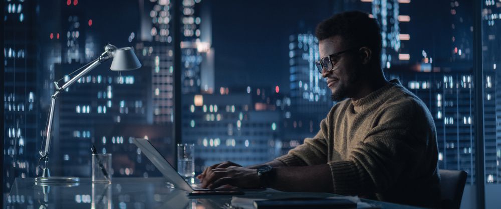 Successful Black Businessman Working on Laptop Computer in Big City Office in the Evening.