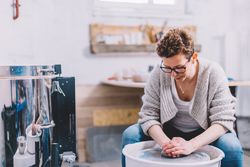 Woman potter shaping vessel on wheel