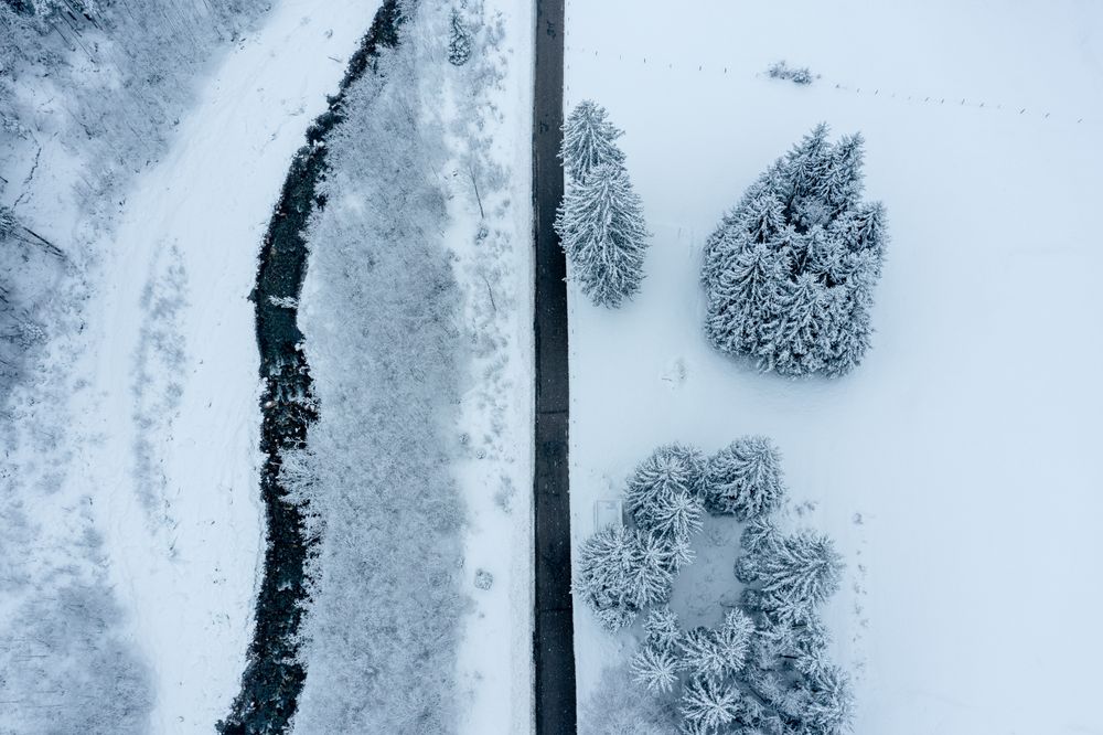 Winter road near mountain river in snowy scenery, drone aerial view