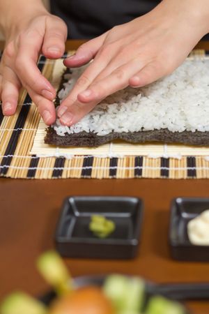 Hands of woman chef flattening rice to roll sushi in a nori seaweed sheet, vertical