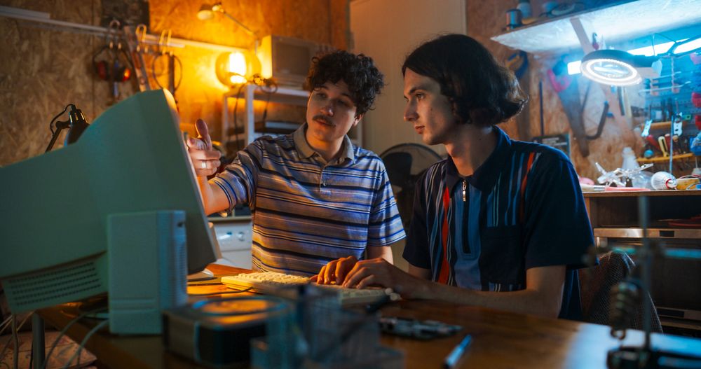 Portrait Of Male Tech Startup Founders Using Old Desktop Computer In Retro Garage In The Evening.