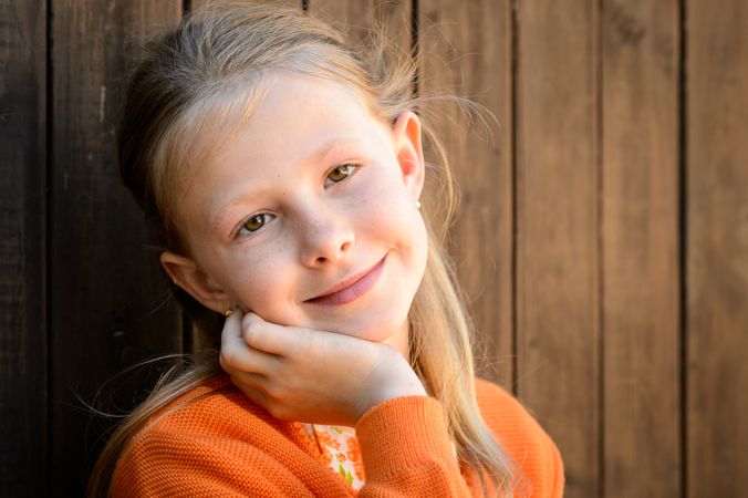 Smiling girl touching cheek against wooden wall