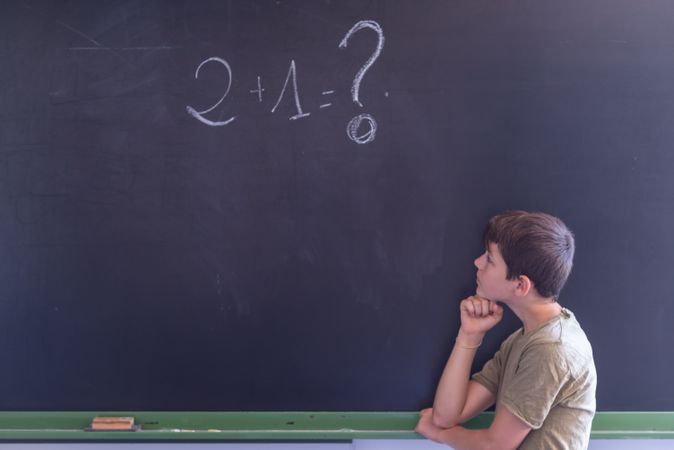 Boy standing at board with math question written in chalk