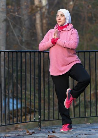 Woman in light hijab and and pink hoodie doing yoga outdoor