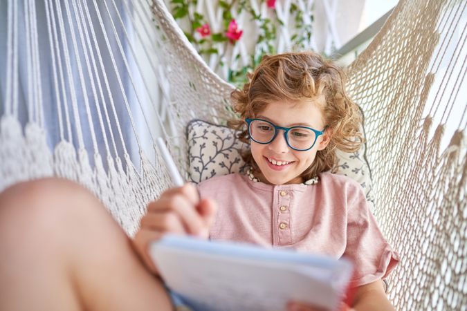 Happy boy taking notes in notepad in hammock