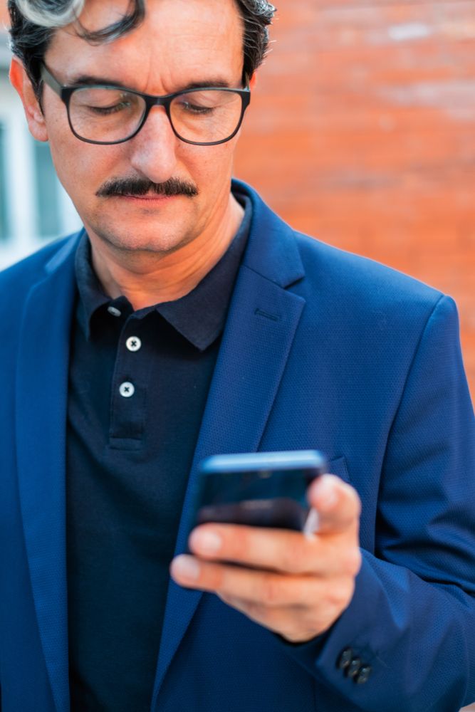 Mature businessman in blue jacket using smartphone