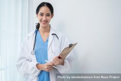 Smiling Asian doctor standing in light hospital room with copy space 49LZE5