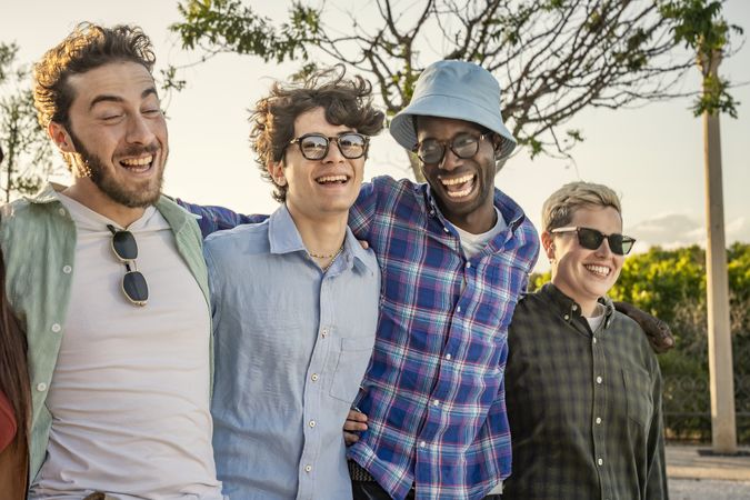 Close-up of four happy diverse friends laughing together outdoors.