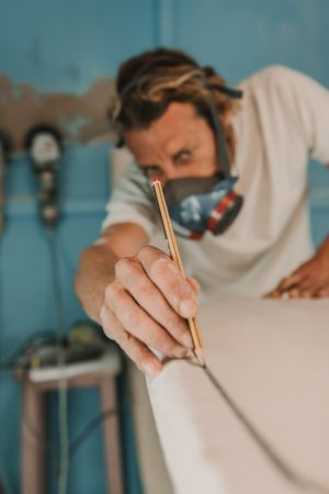 Man in respirator measuring surf board in workshop