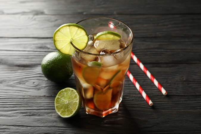 Glass of cold cola with citrus and ice on wooden table, space for text