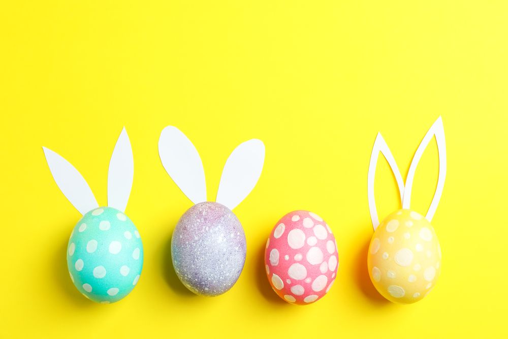 Decorated Easter eggs with cute bunnies ears on yellow background. Space for text