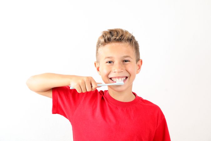 Boy with toothbrush on blank background, space for text
