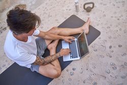 Male sitting on mat and browsing laptop