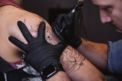 Master doing tattoo on forearm of male customer